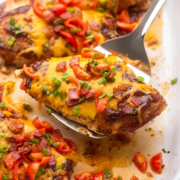 close up of spatula scooping baked chicken breast out of pan.