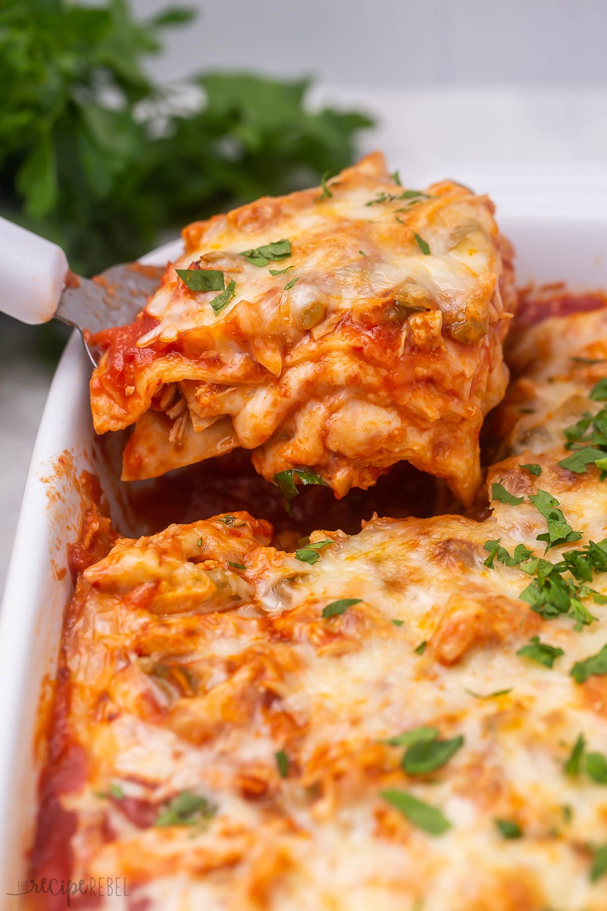 chicken enchilada casserole being scooped out of baking dish.