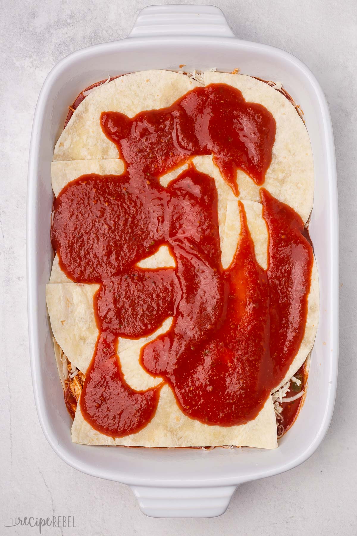 Top view of enchilada casserole being layered into a dish. 