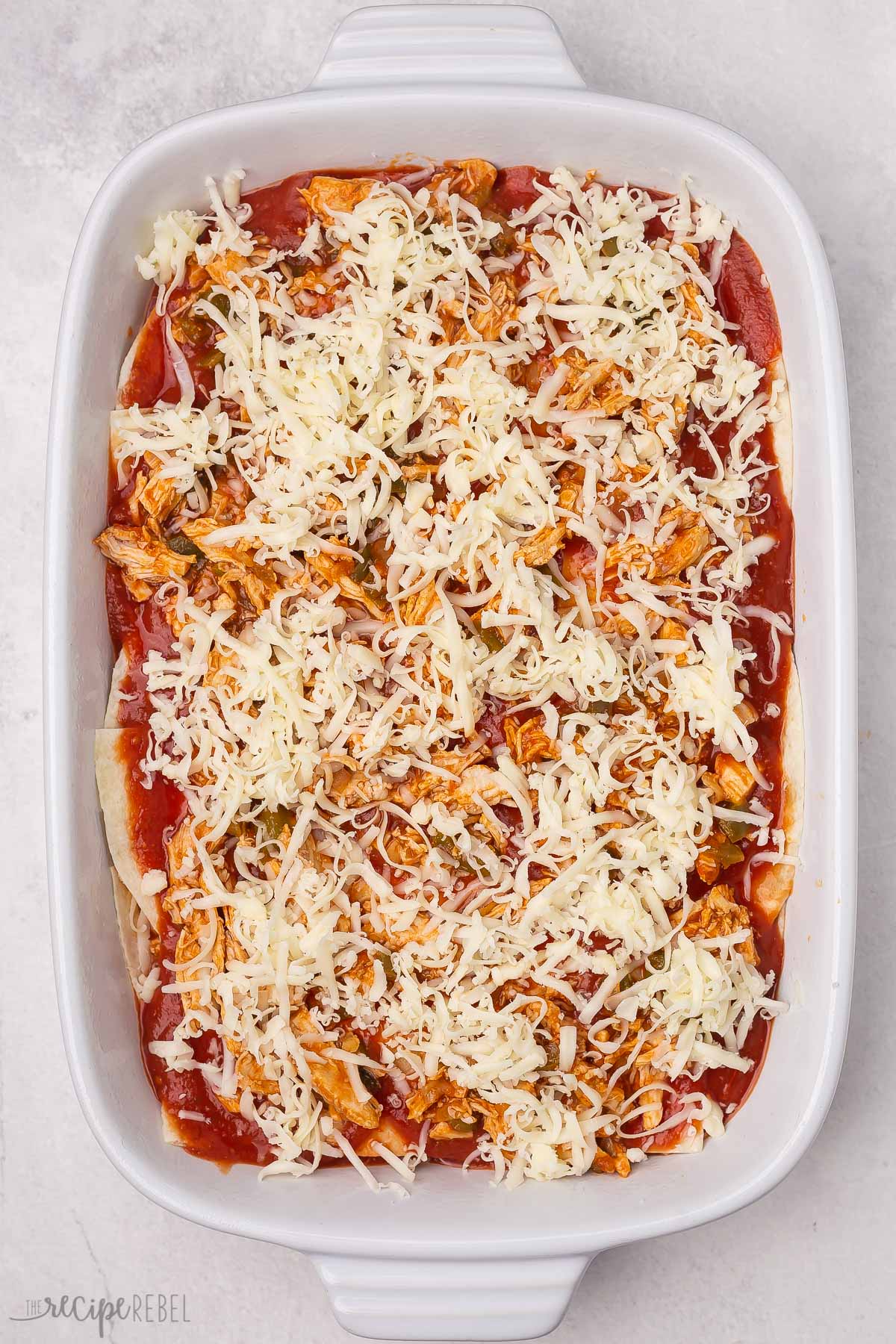 Top view of uncooked enchilada casserole with cheese on top.
