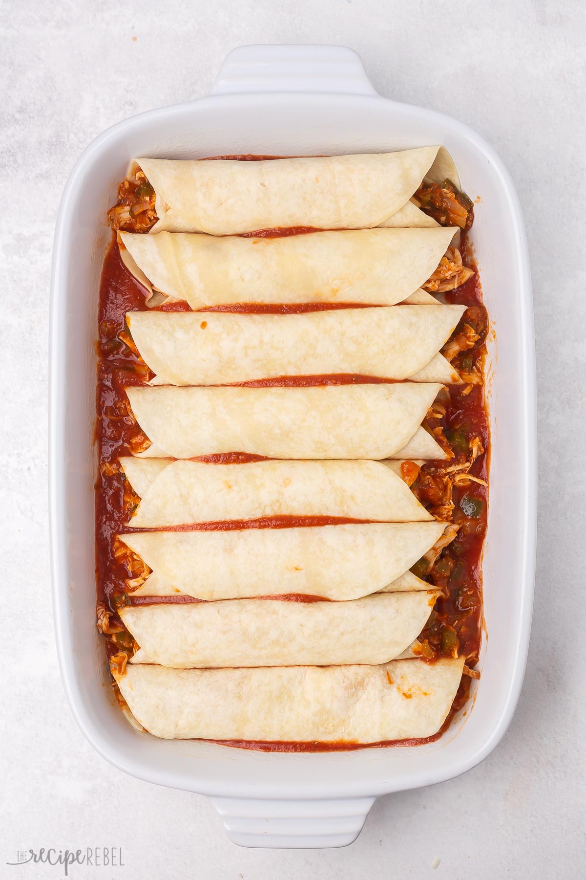 overhead shot of a white pan full of enchiladas and sauce.