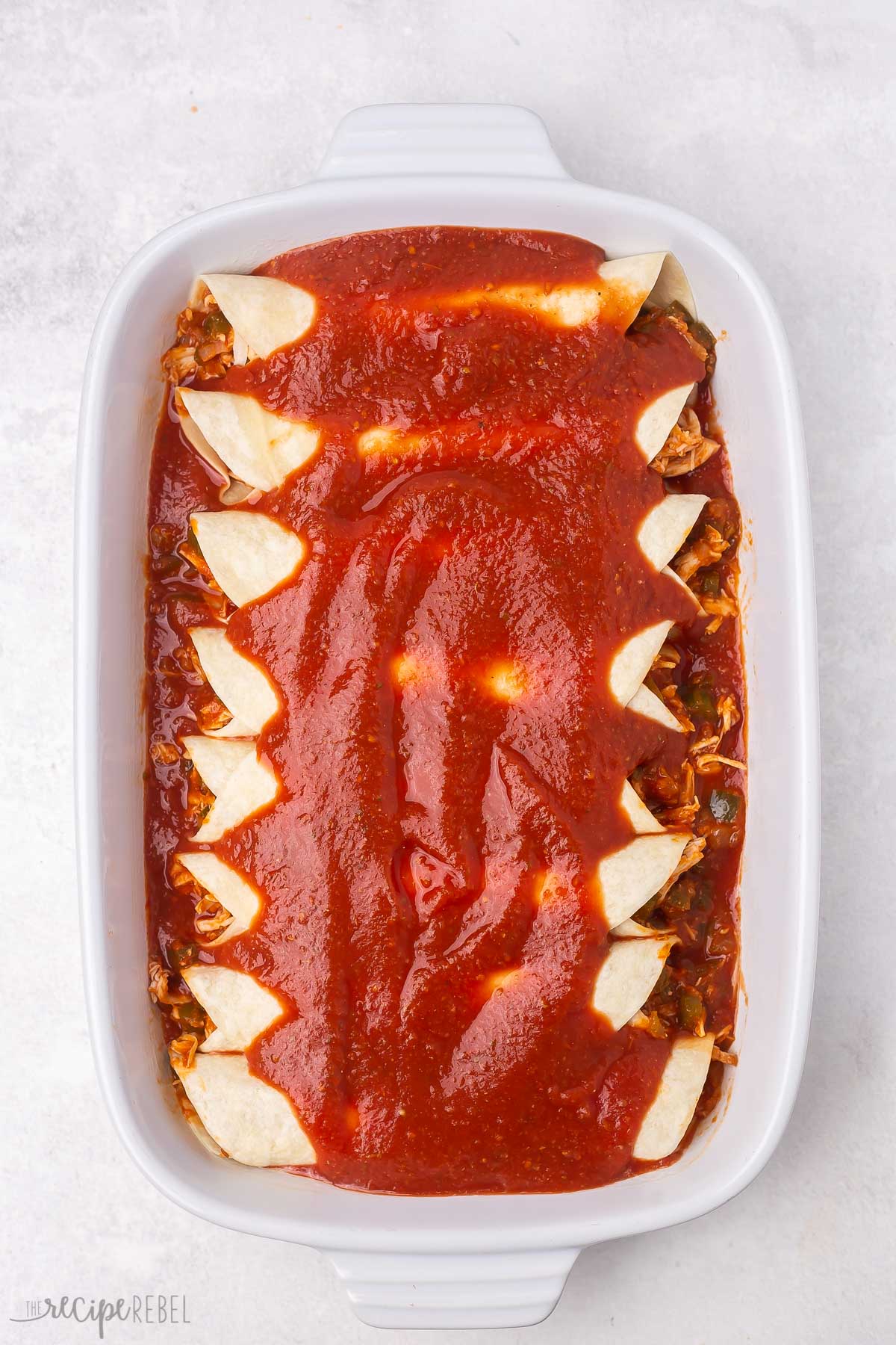 a white baking dish filled with enchiladas and sauce on top.