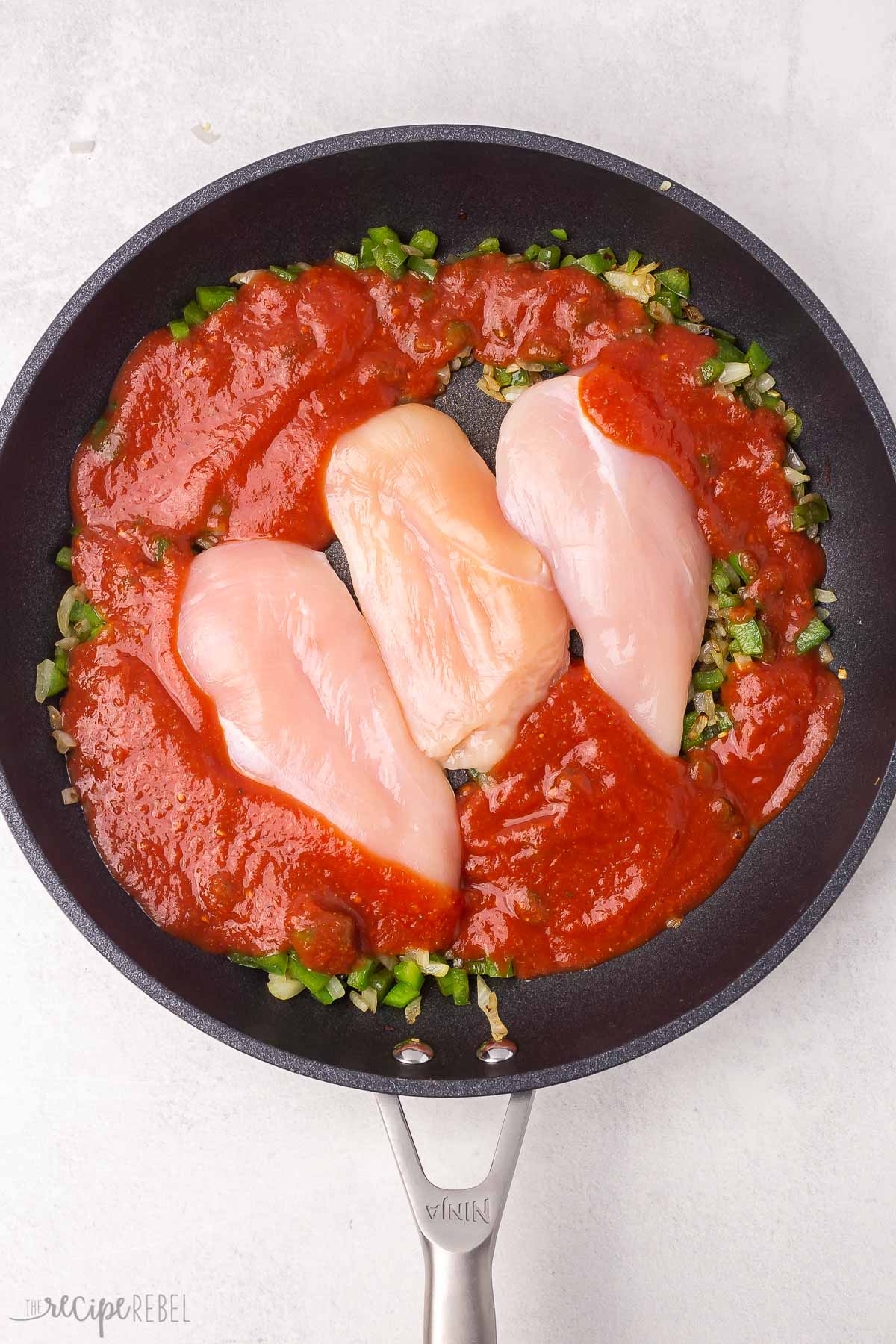 three chicken breasts and sauce lying in a black frying pan.
