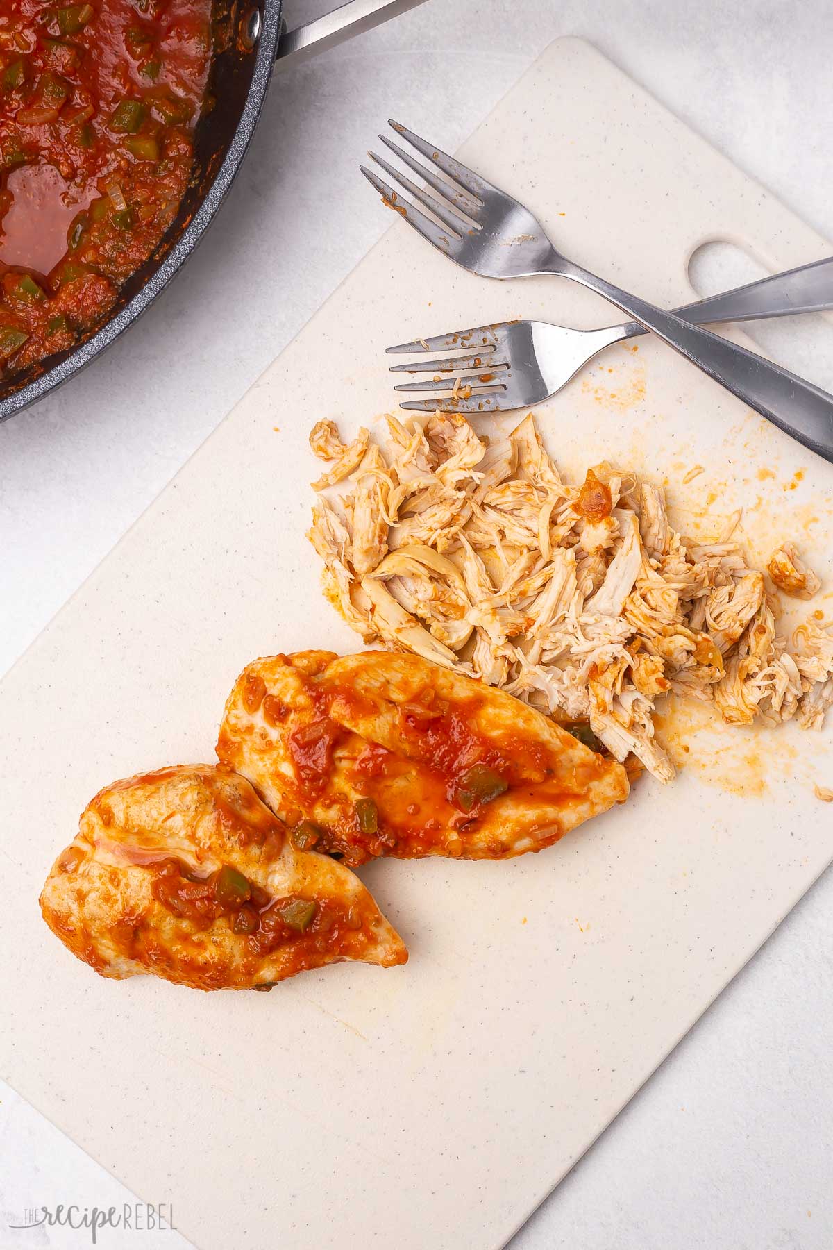 two cooked chicken breasts and shredded chicken on a cutting board.