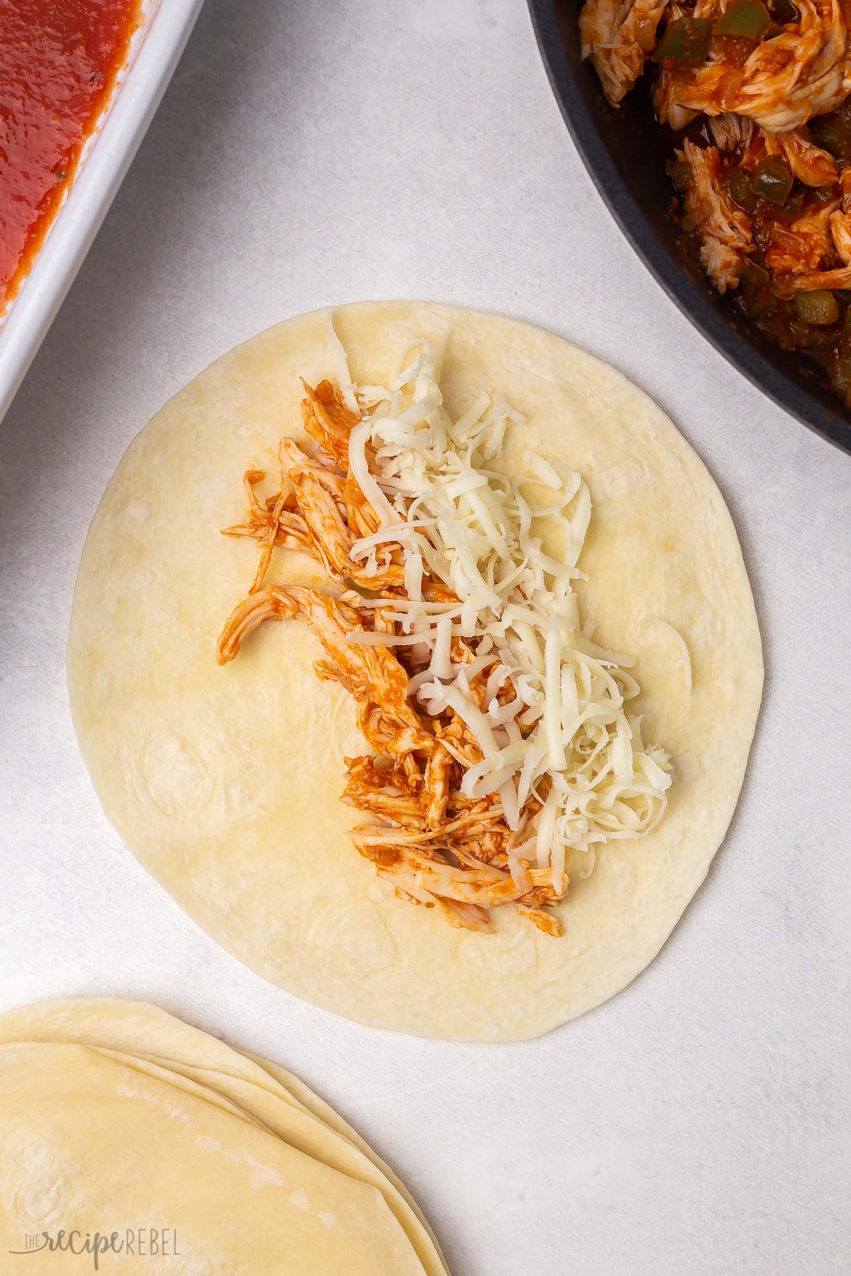 tortilla with shredded chicken and mozzarella lying on a grey surface.