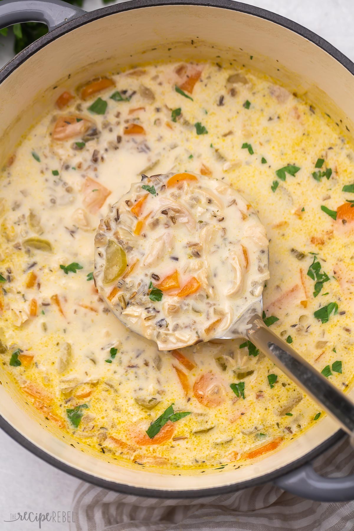 Top view of large pot with chicken wild rice soup in it and a ladel scooping some out. 