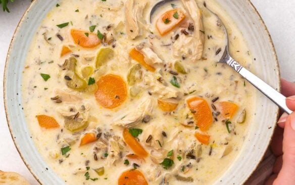 Top view of chicken wild wice soup in a white bowl with a spoon in it.