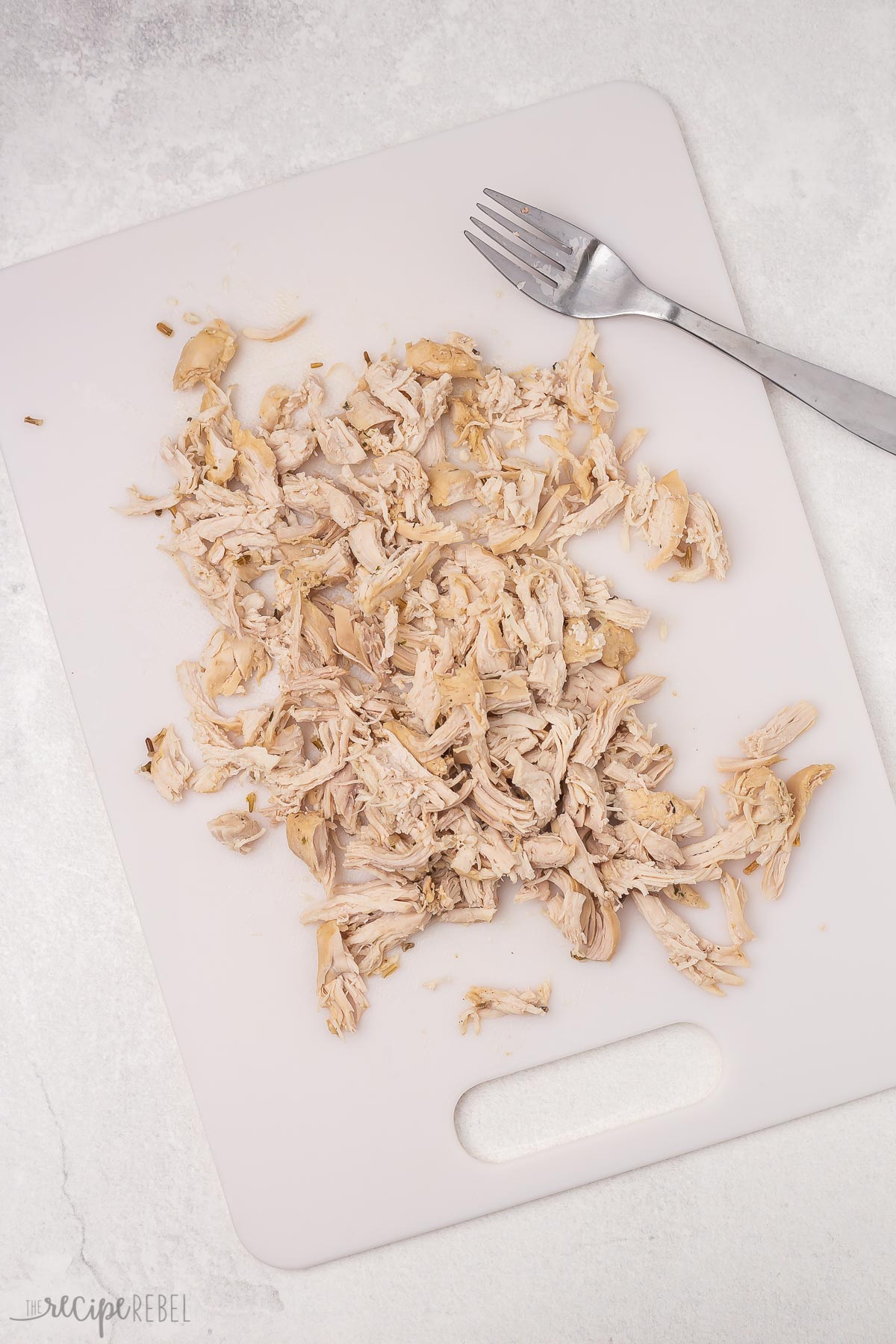 Top view of shredded chicken on a white chopping board. 