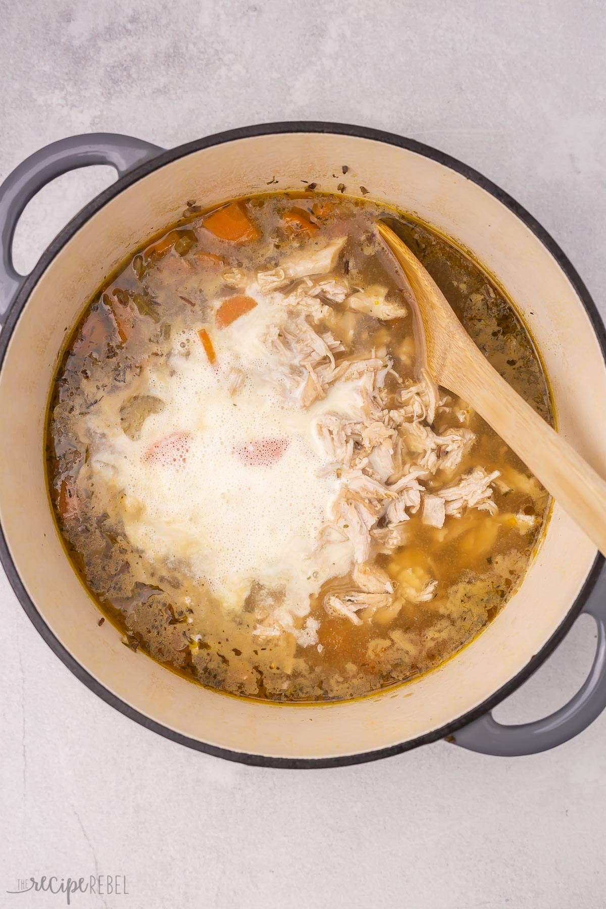 Top view of dutch oven with chicken wild rice soup in it with cream just added, being stirred by a wooden spoon. 