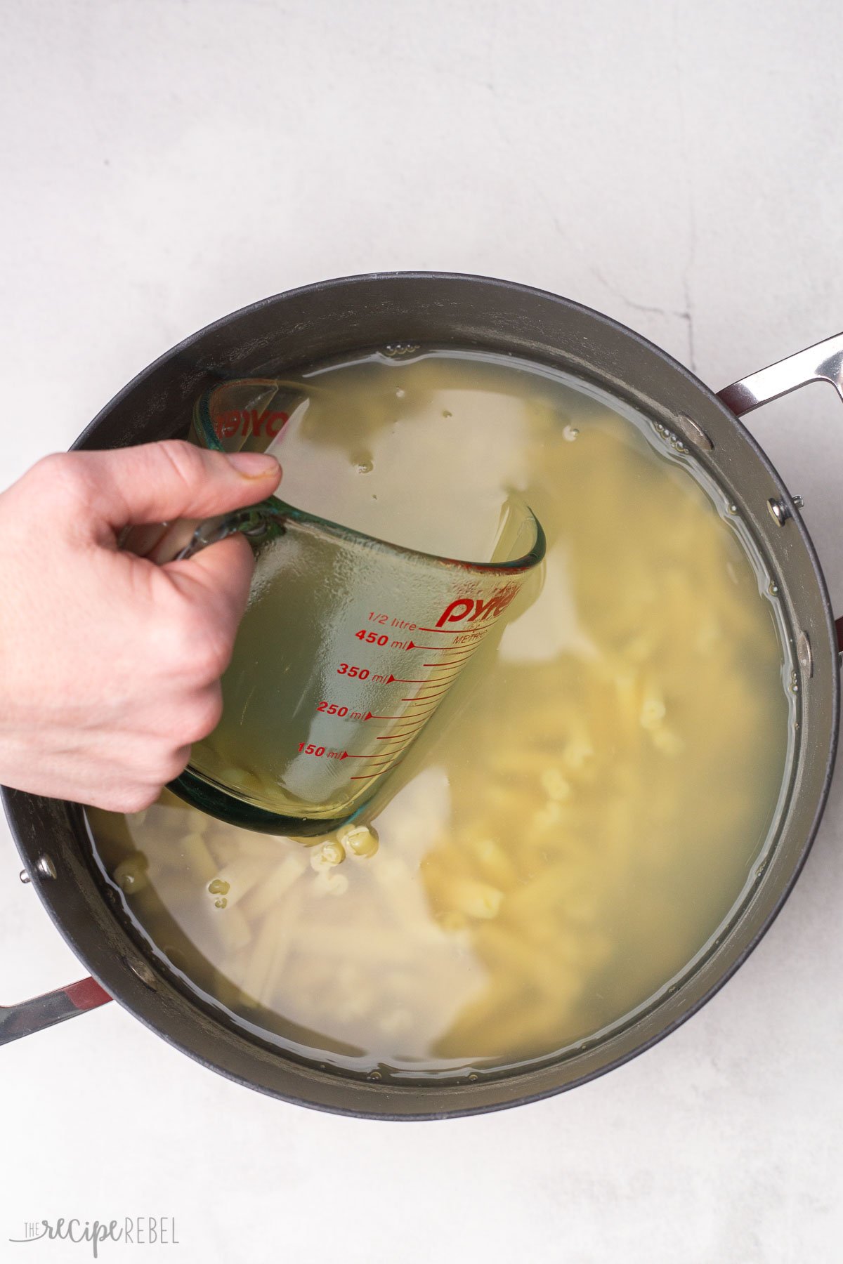 measuring cup scooping pasta water out of pasta pot.