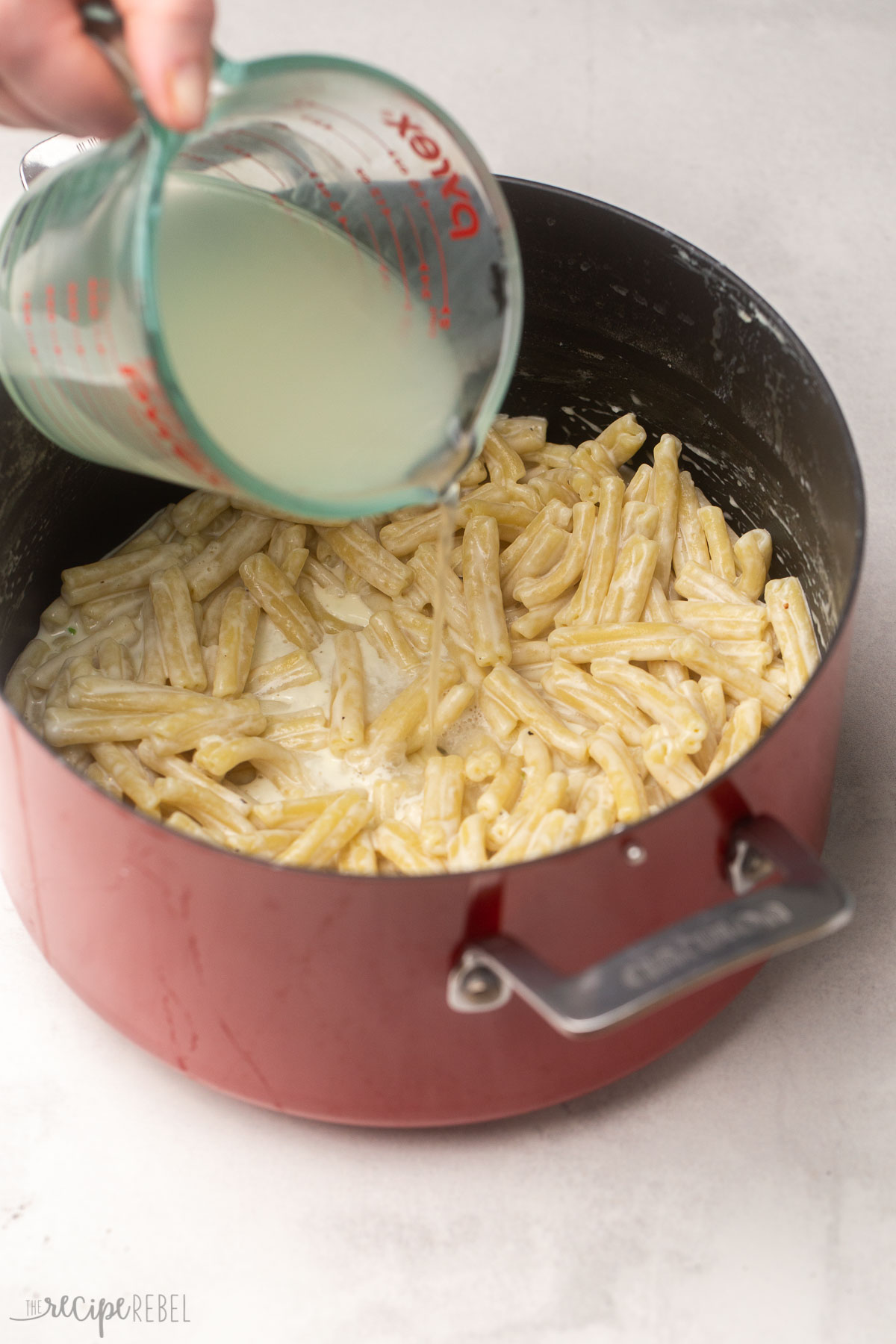 reserved pasta water being poured into cooked pasta in a red pot.