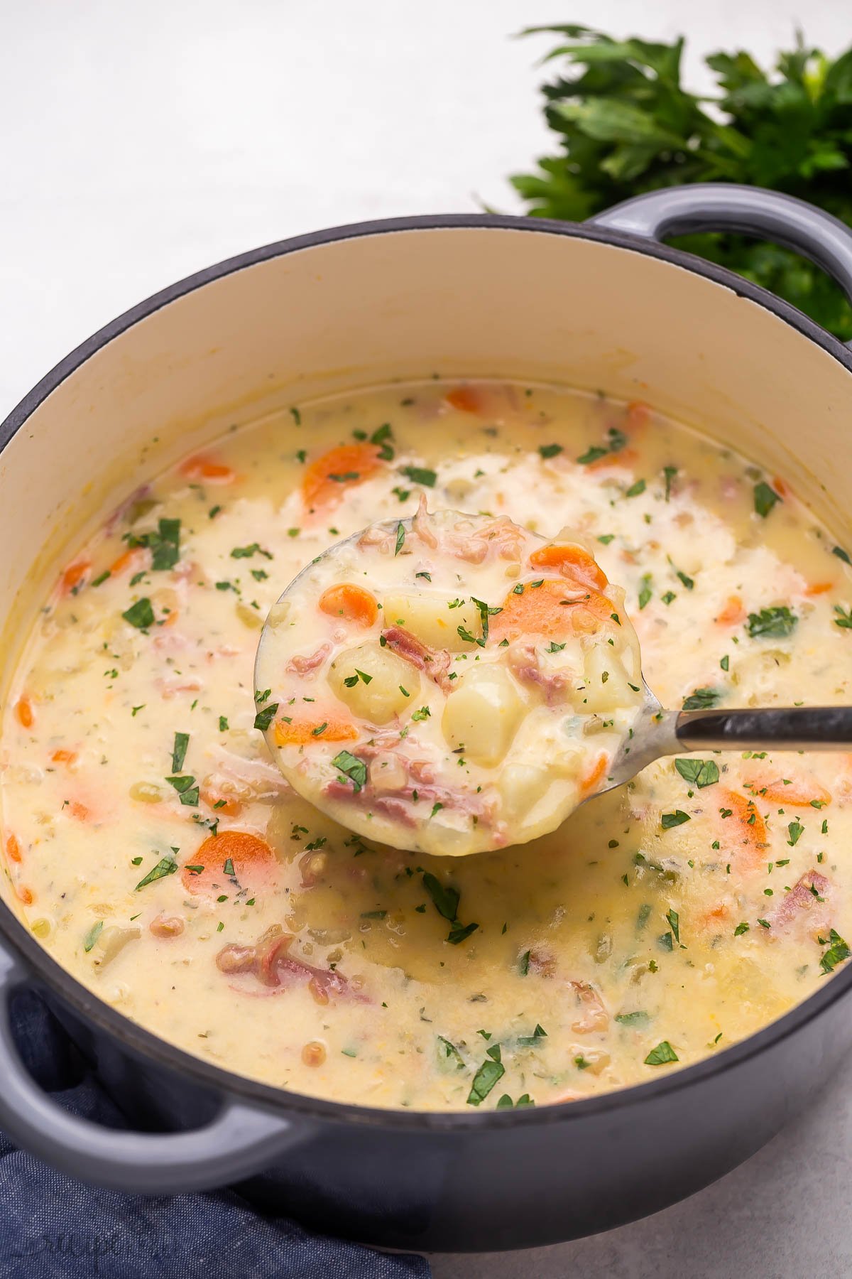Top view of a big pot filled with ham and potato soup with a ladle in it.