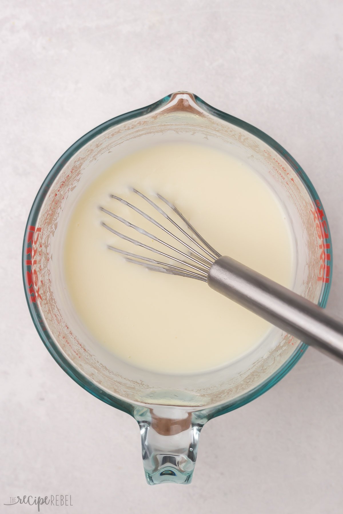 Top view of glass jug with a white sauce and a whisk in it.