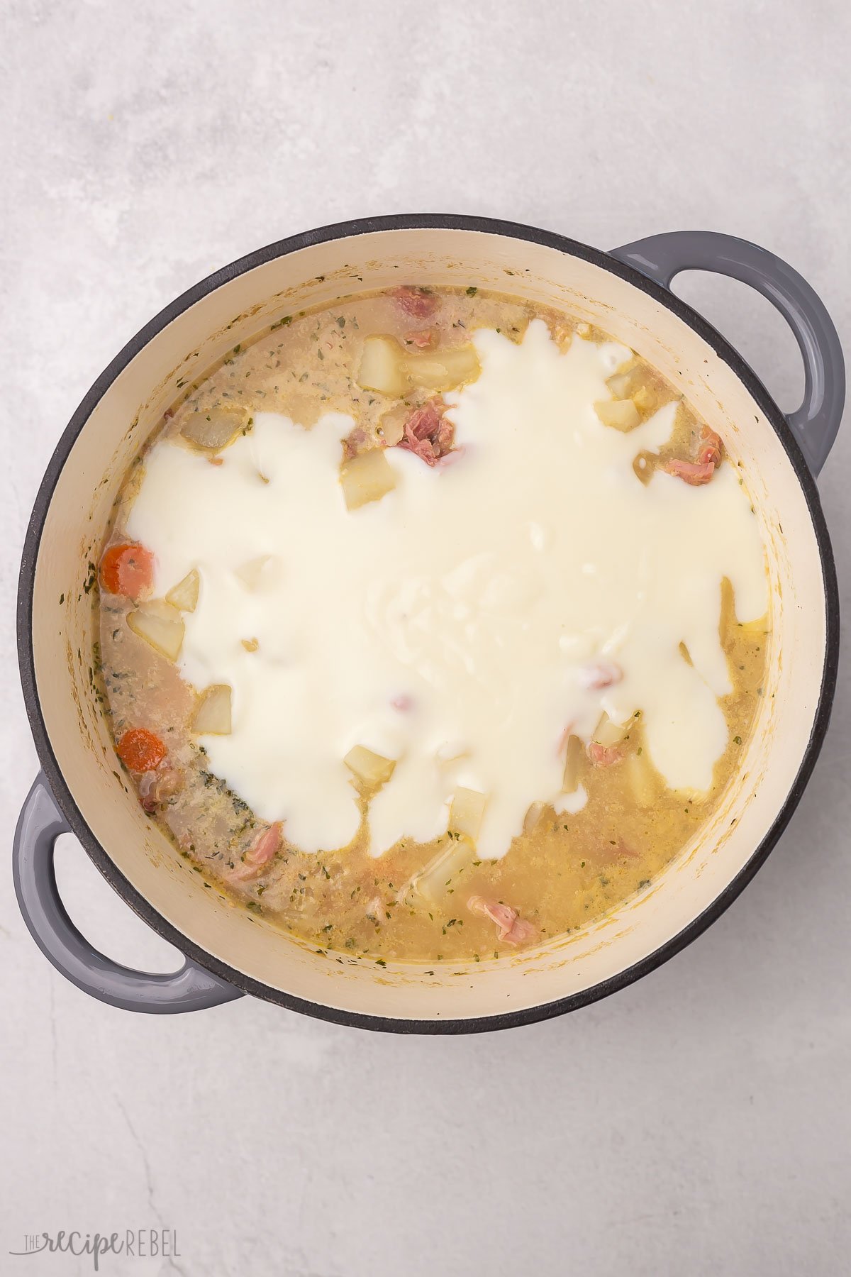 Top view of dutch oven with ham and potato soup in it and thickened milk being added in.