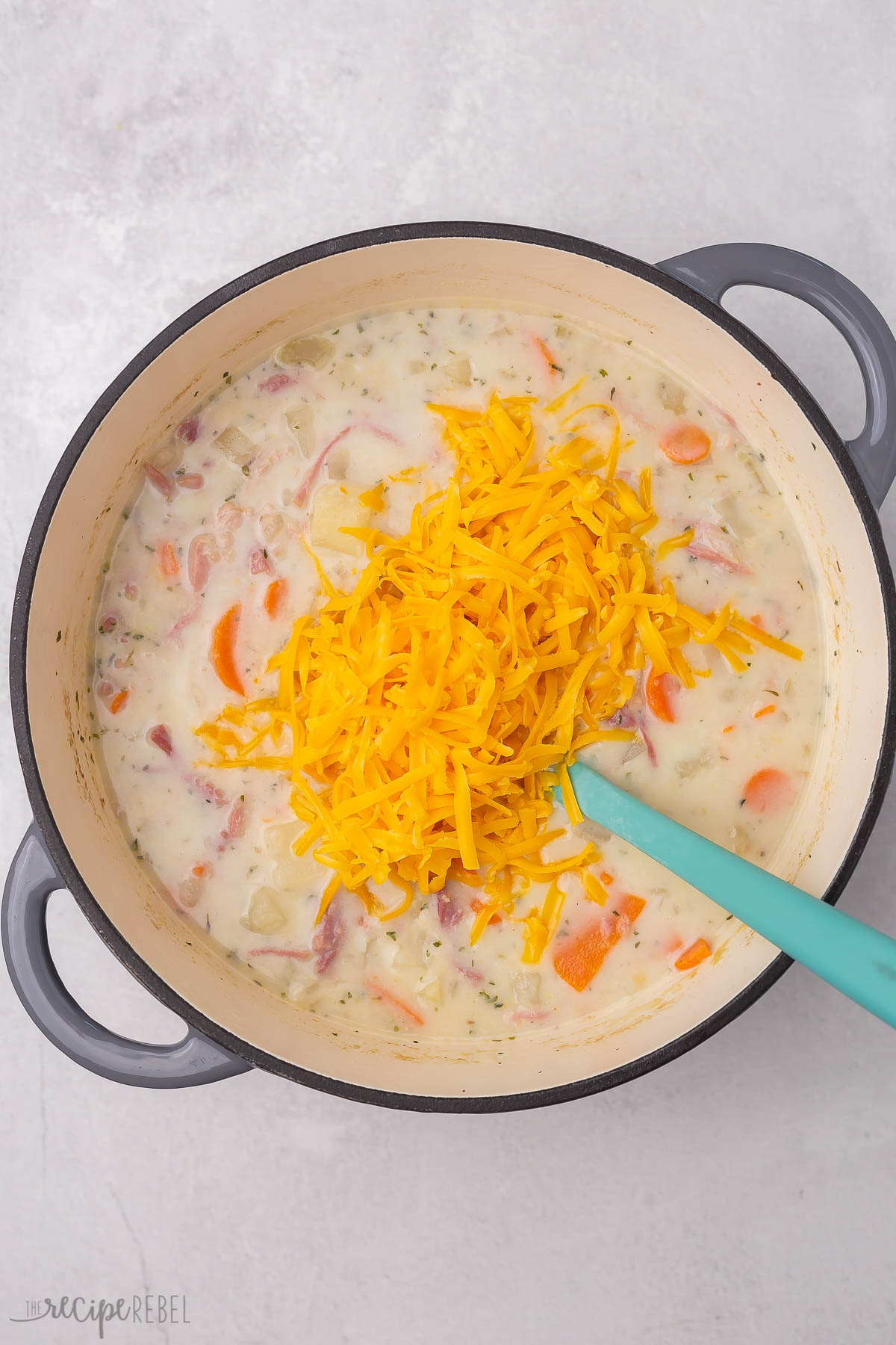 Top view of dutch oven with creamy ham and potato soup in it with shredded cheese being added on top.