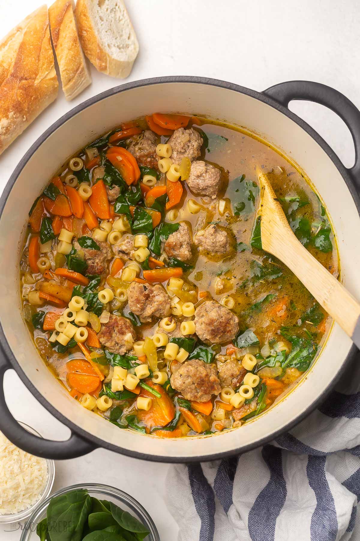 Italian Wedding Soup is loaded with homemade Italian meatballs, pasta, savory vegetables, salty parmesan, and classic Italian seasoning. It's one of our favorite soups for lazy winter days, but it's great for hearty dinners any time of year. #soup #recipe | dinner ideas | dinner recipes | soup recipes | meatball recipe | healthy dinner | easy recipes top view of cooked soup in pot with bread and wooden ladle in pot.