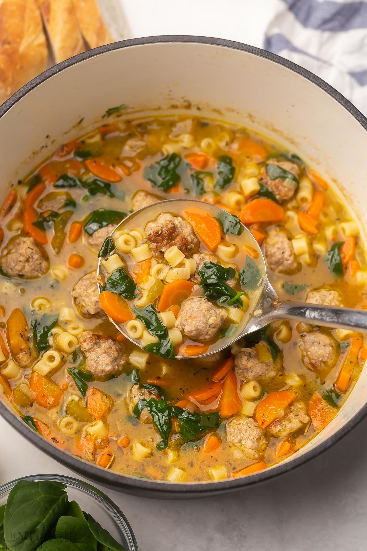 Top view of a large pot of Italian wedding soup with full scoop being lifted out.