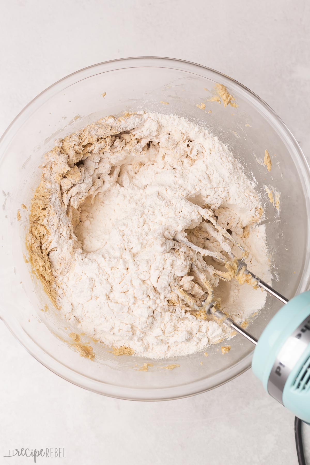 flour and other ingredients in glass bowl with mixer beside.