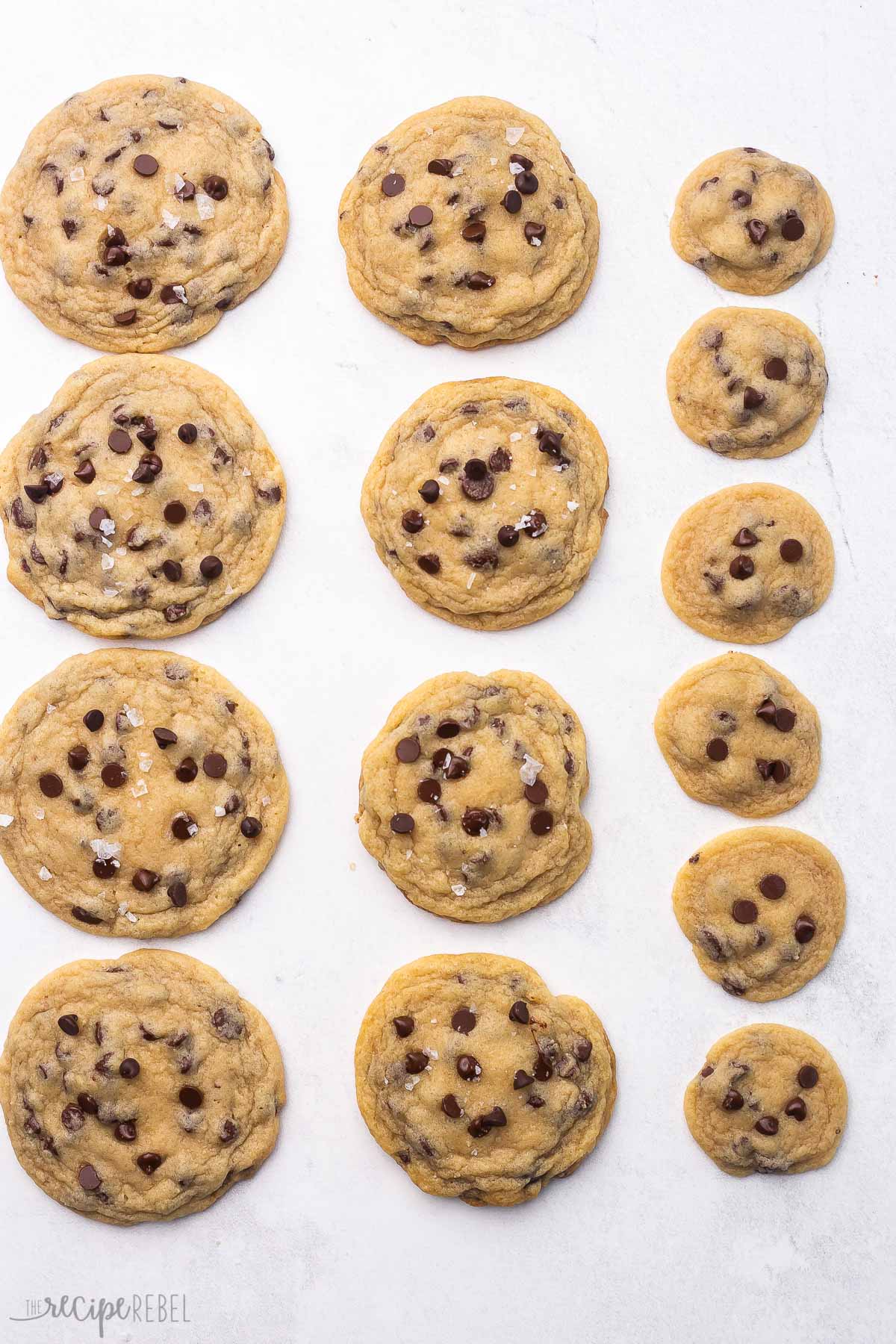 overhead view of baked chocolate chip cookies in various sizes on grey surface.