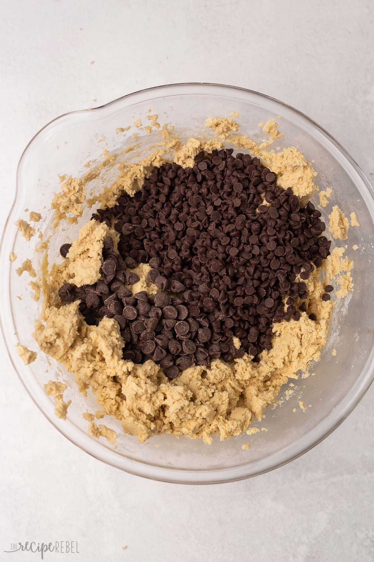 mixed cookie ingredients in glass bowl with chocolate chips on top.