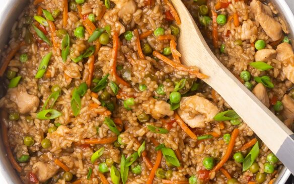 close up of cooked teriyaki chicken and rice with wooden ladle in pan.