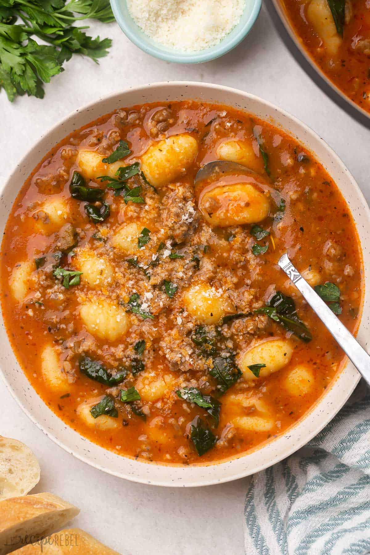 This Italian Sausage Gnocchi Soup will turn up the heat on those cold days. There is so much flavor in this soup with Italian sausage, tons of seasonings, and a parmesan rind, you can even add red pepper flakes for an extra kick! #soup #recipe | dinner recipes | soup recipe | italian sausage | gnocchi | dinner ideas overhead image of a bowl of sausage gnocchi soup with spoon stuck in.
