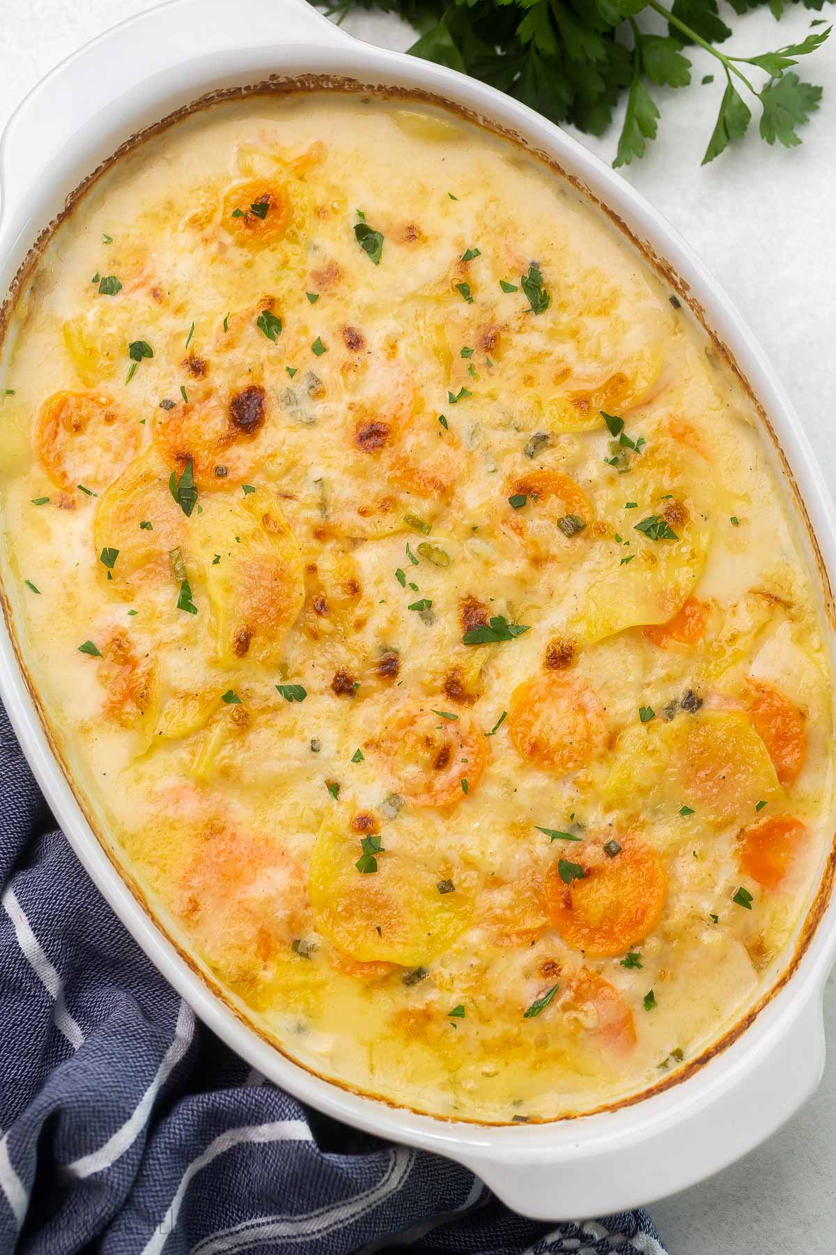 Top view of scalloped potatoes and carrots in a white dish.