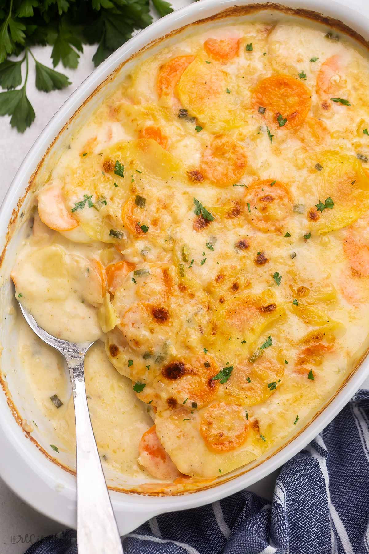 top view of baked scallop potatoes in white dish with spoon.