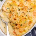 close up square shot of baked scalloped potatoes and carrots in white dish.