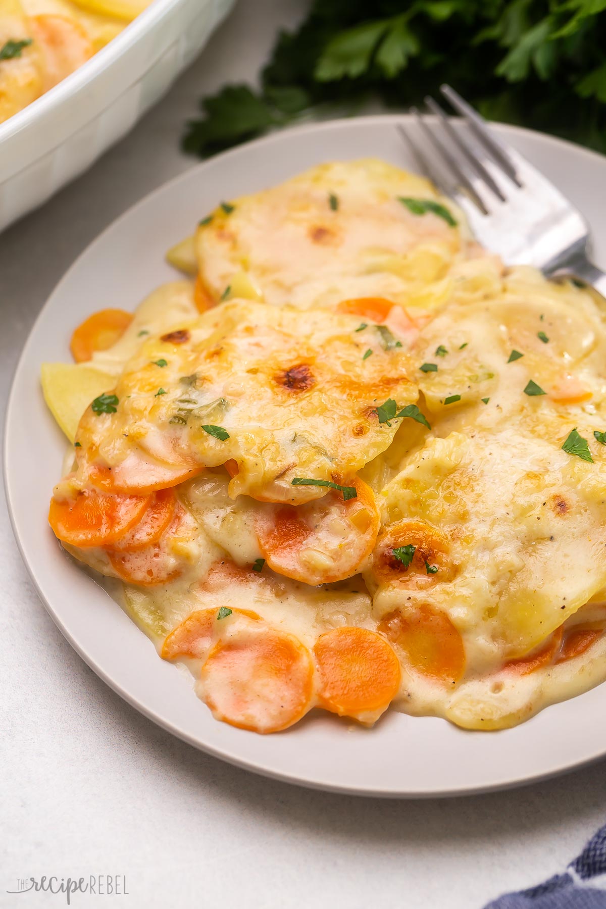 Top view of a plate of scalloped potatoes and fork, garnished with chopped parsley.