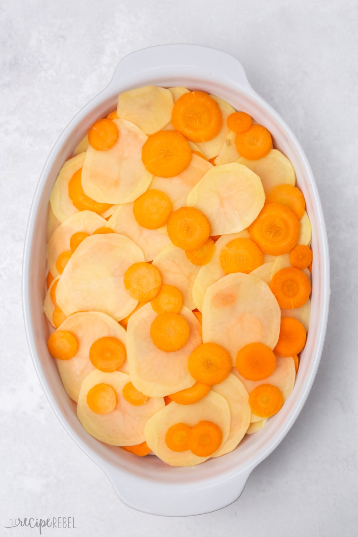 Top view of white dish with scalloped potatoes and carrots layered in it. 