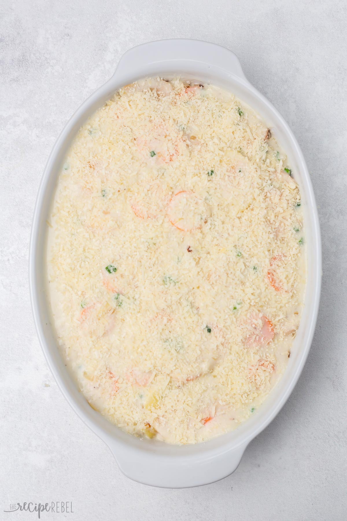 Top view of white dish with unbaked scalloped potatoes and carrots.