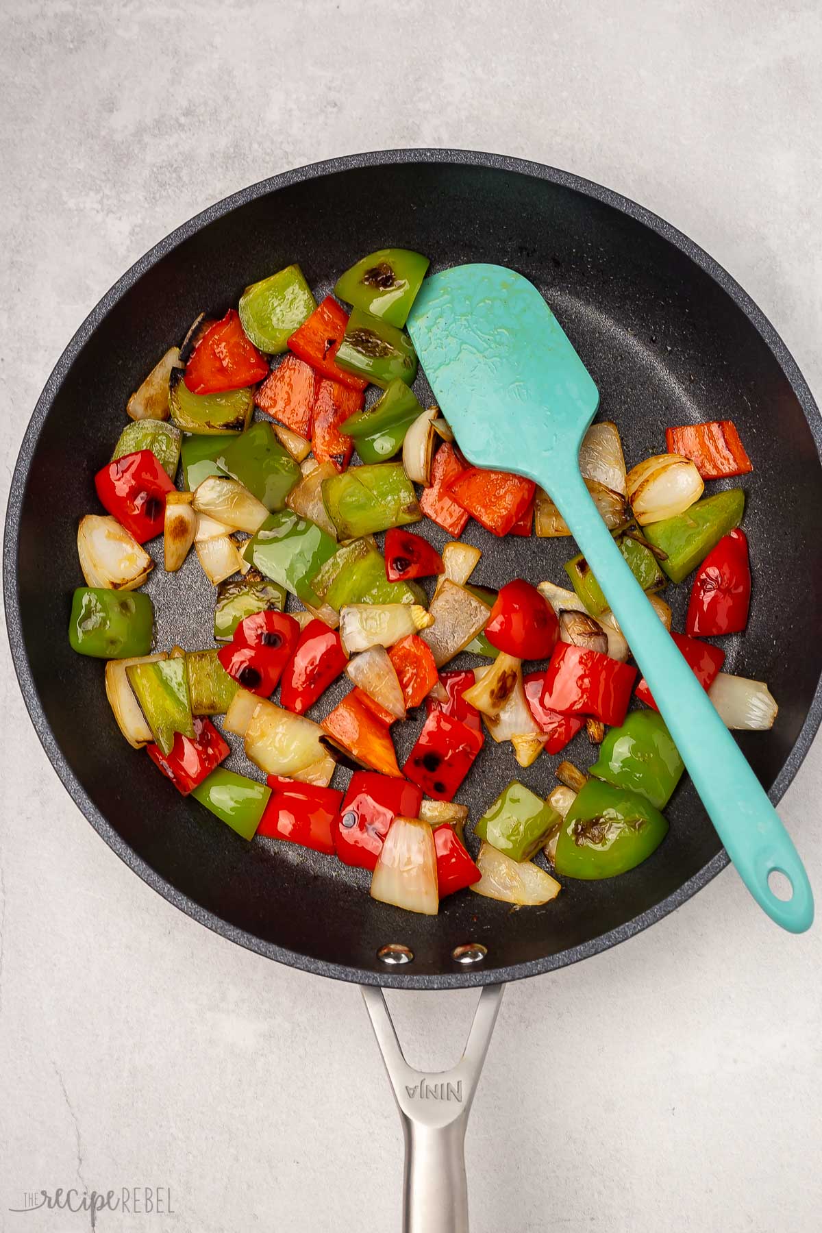 Top view of onion, red, and green bell peppers being fried in a pan. 