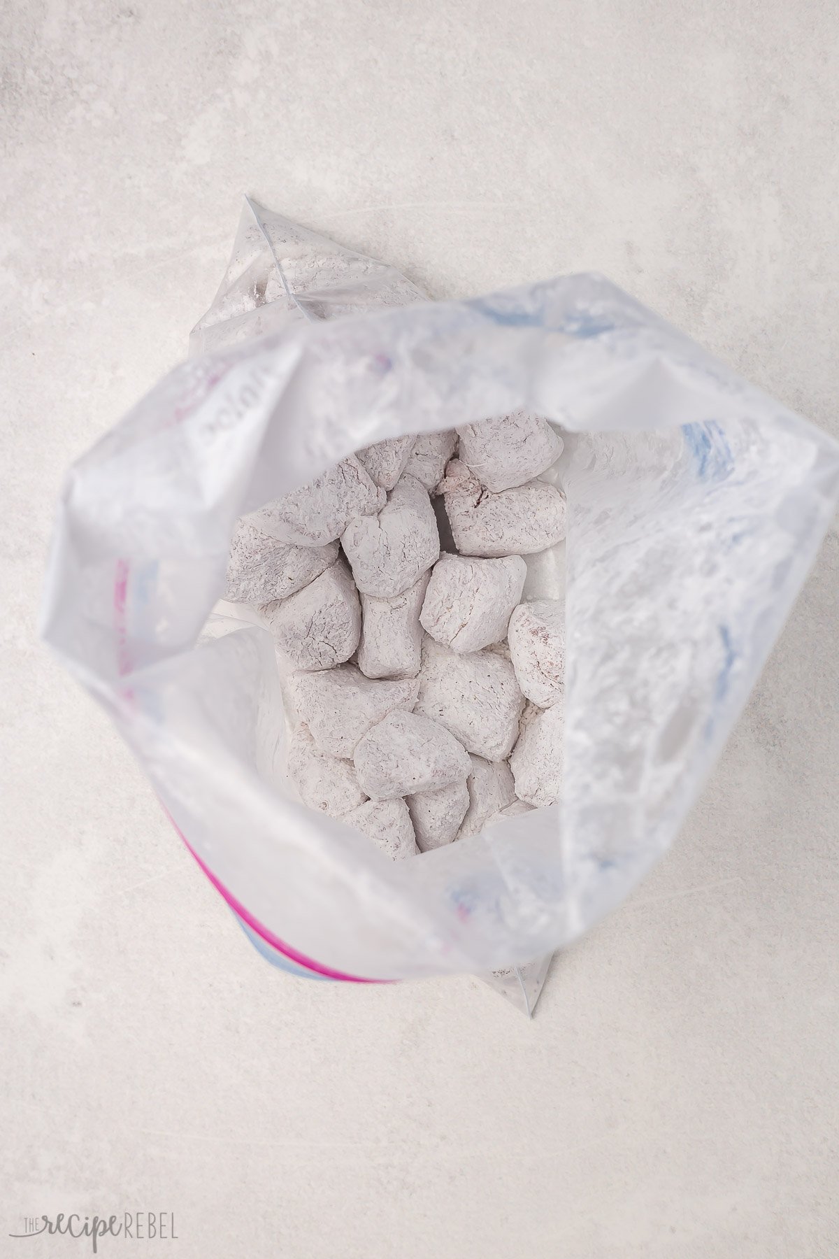 Top view of an open Ziploc bag that has white cubes of pork coated in cornstarch in it. 