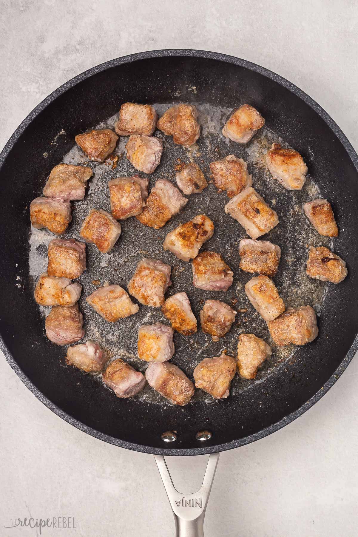 Top view of a black pan with crispy pork being fried in it. 