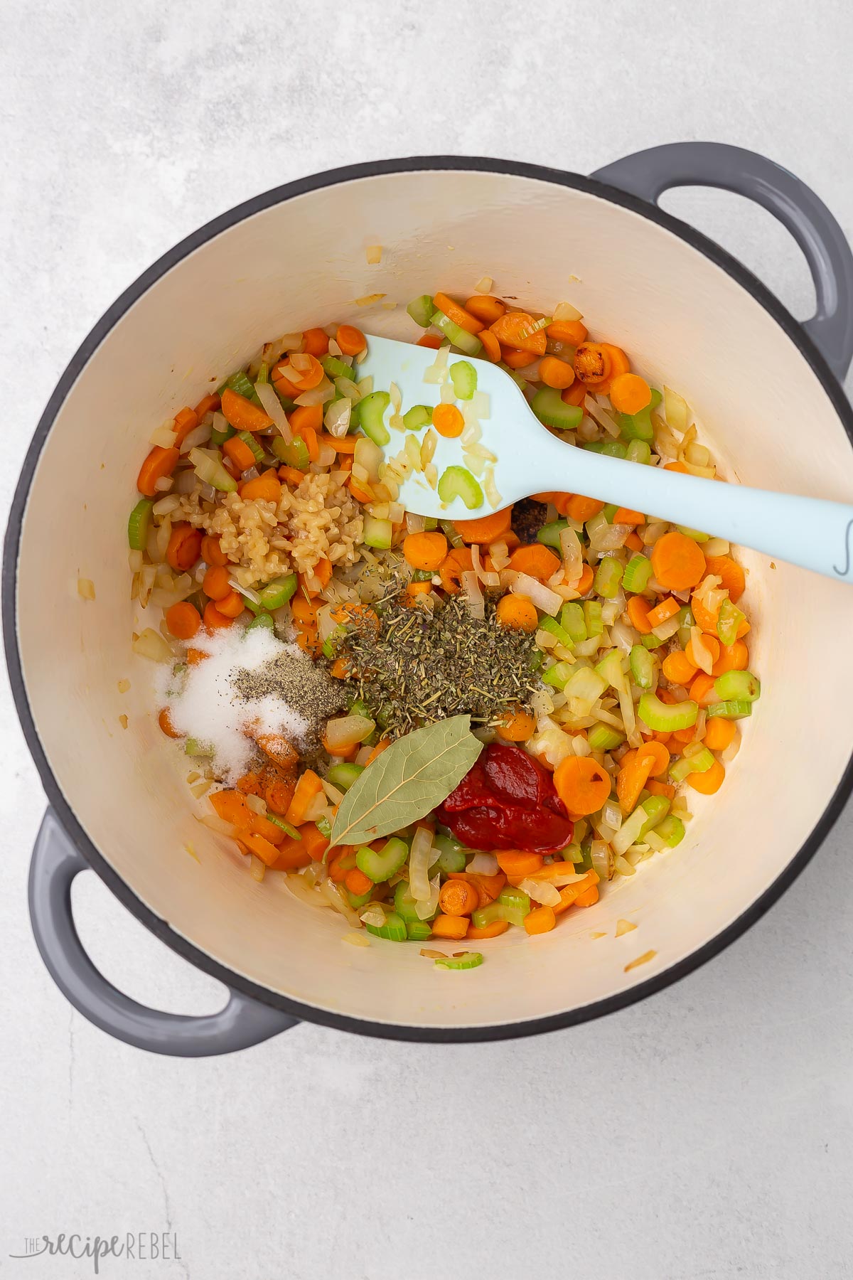 Top view of a pot with vegetables, seasoning and a bay leaf in it for making soup.