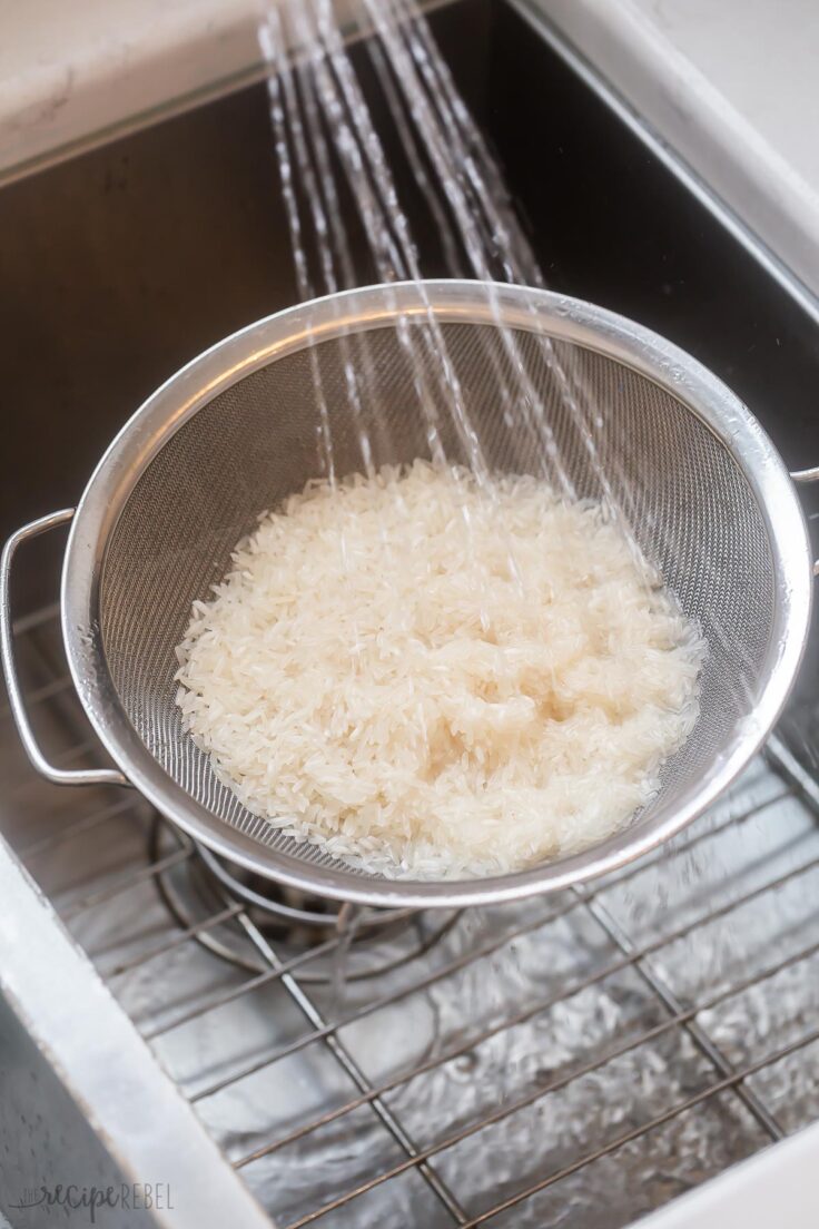 white rice in stainless steel strainer being rinsed.