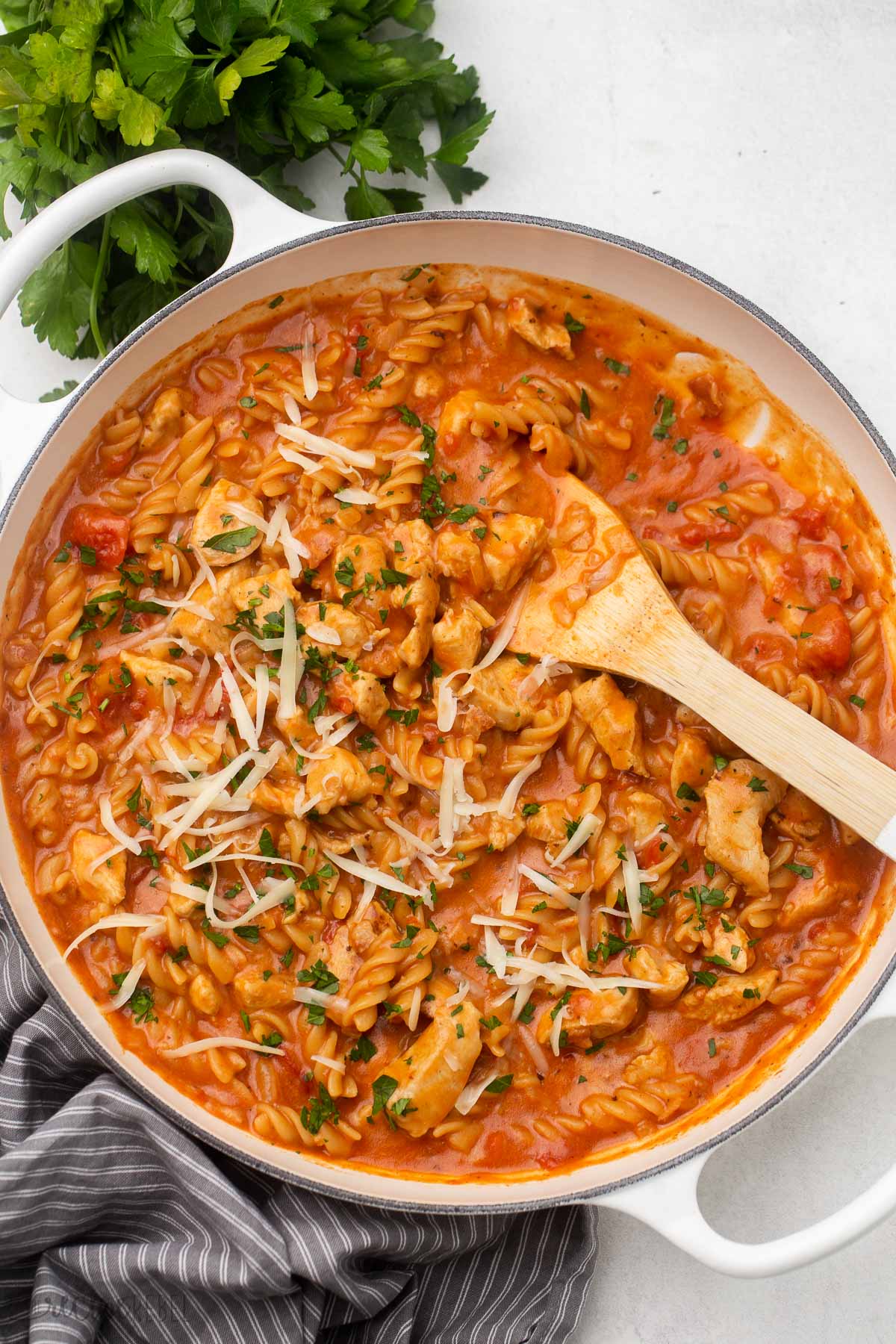 overhead view of white dutch oven full of bbq chicken pasta with parsley and a wooden spatula.