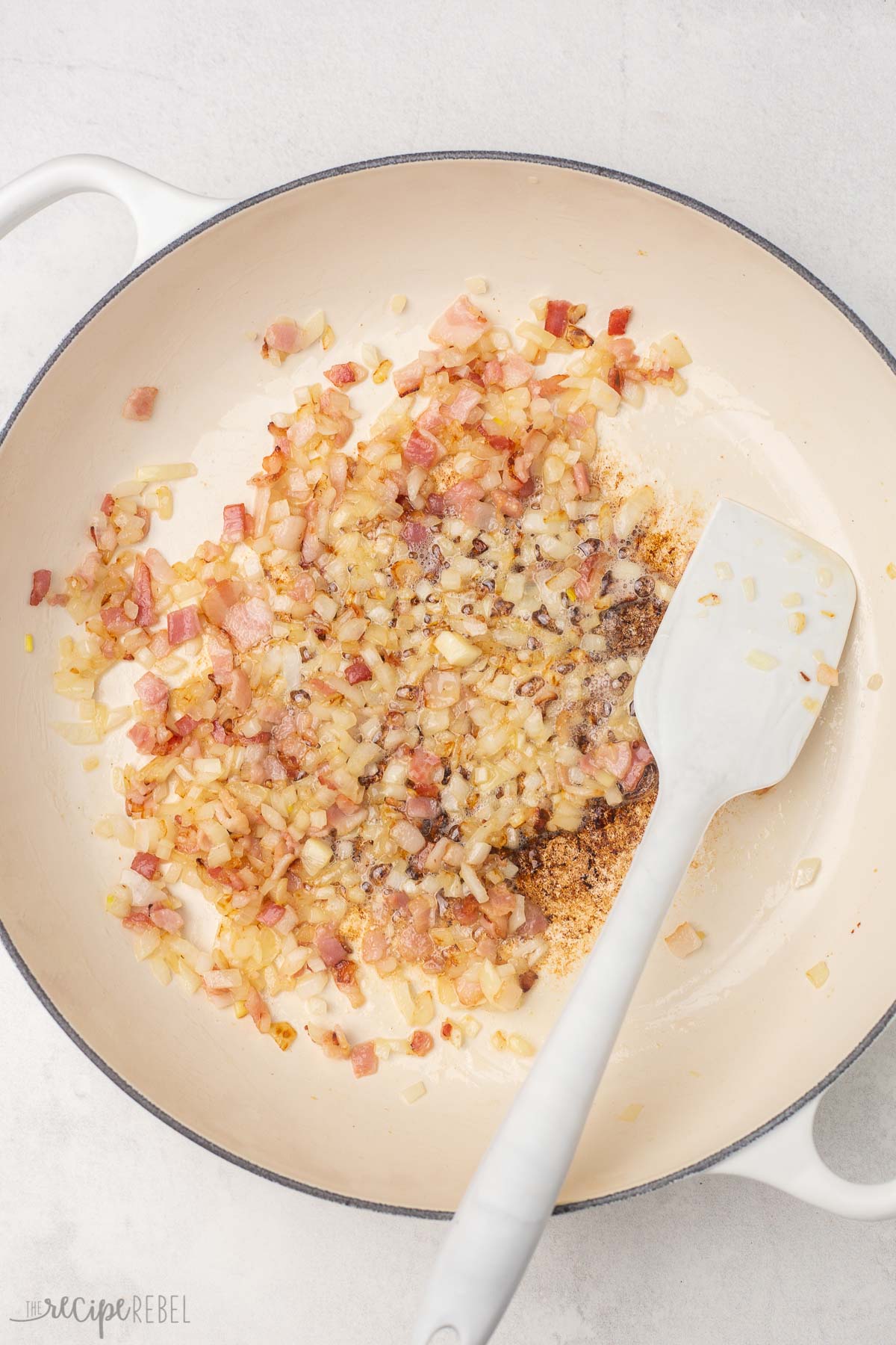 white dutch oven with cooked bacon, onion, and spices.