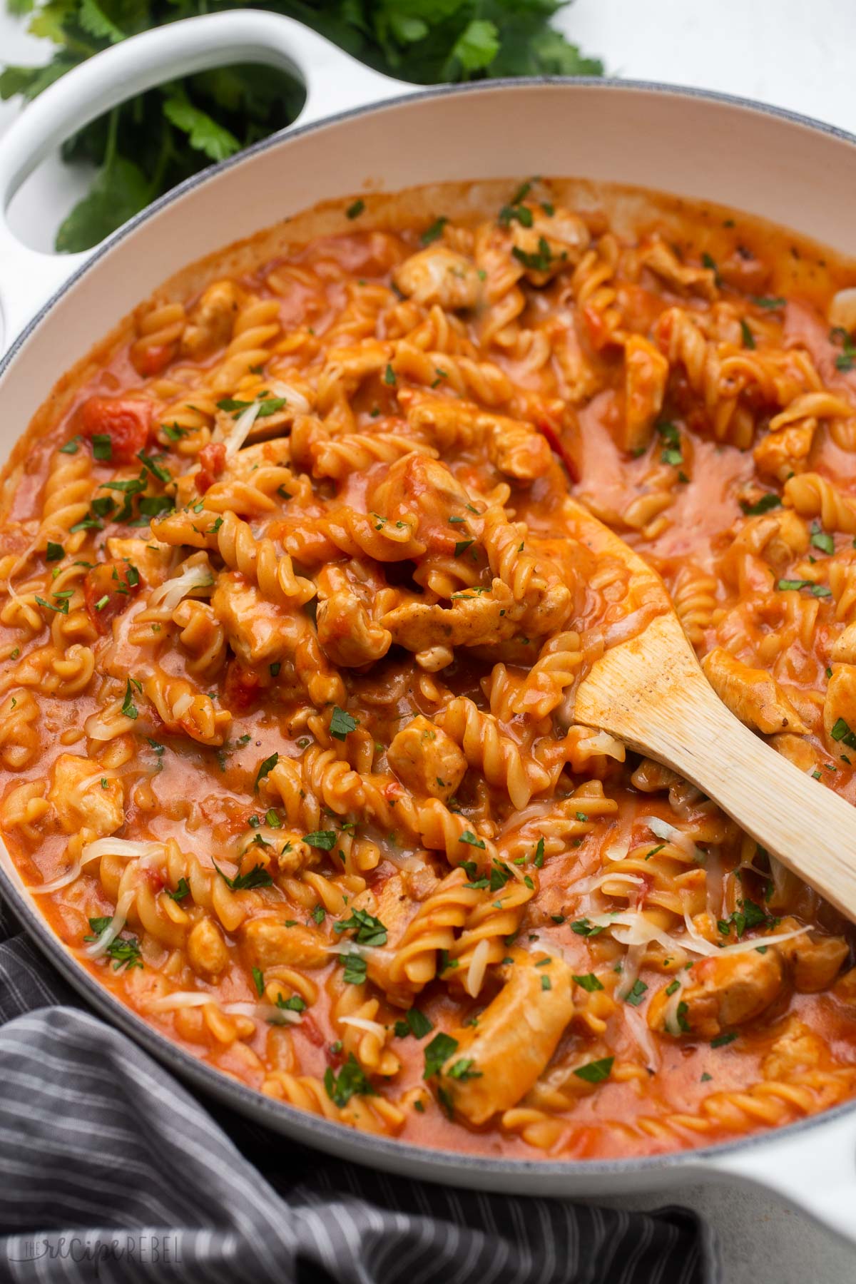 wooden spatula scooping bbq chicken pasta out of white dutch oven.