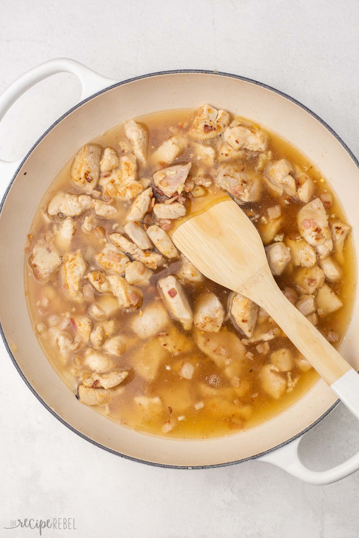 overhead view of chicken broth added to cooked ingredients in white dutch oven.