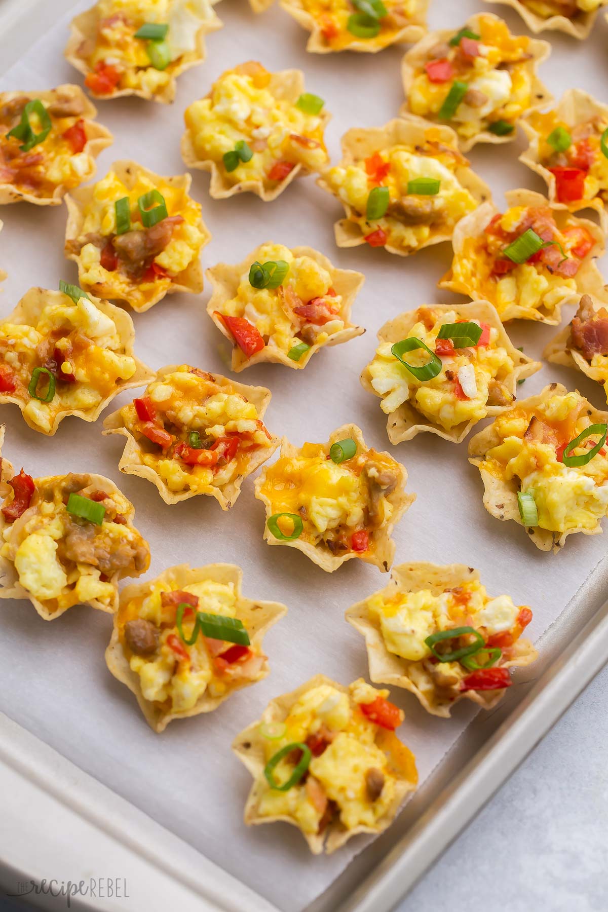 Mini tortilla chips stuffed with delicious sausage, fluffy scrambled eggs, sweet bell peppers, and cheese, these Breakfast Taco Bites are mini mouthfuls bursting with Mexican flavors! They are breakfast. They’re lunch. And they're appetizers. And they're so yummy! | breakfast recipe | appetizer recipe | game day | party food | brunch ideas | breakfast recipes Top view of breakfast taco bites on a baking tray lined with parchment paper.