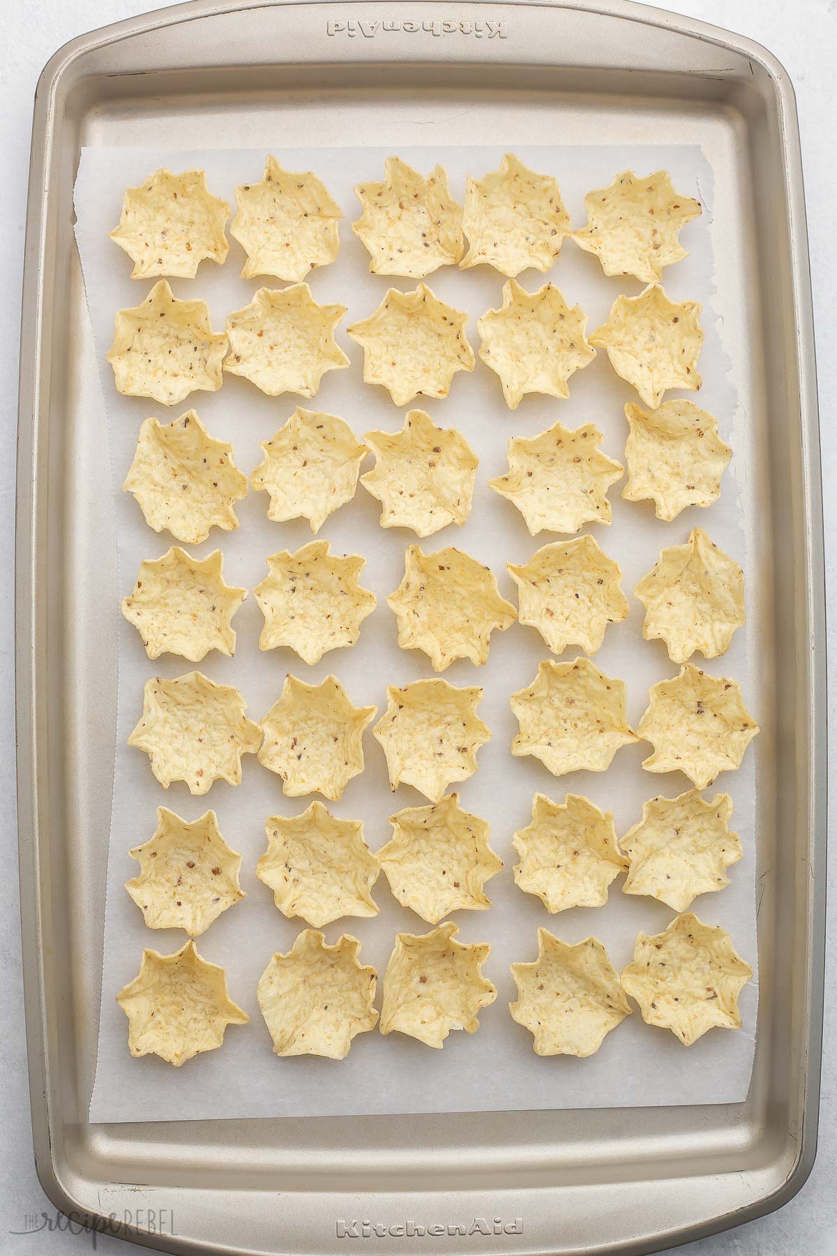 Top view of tortilla chip scoops on a baking tray lined with parchment paper. 