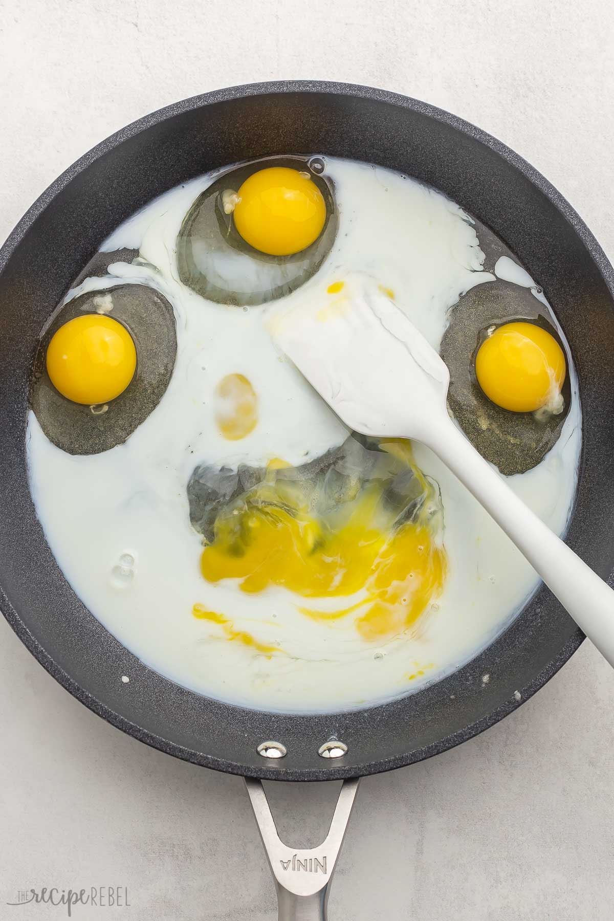 Top view of eggs and milk in a pan with a spatula in it. 