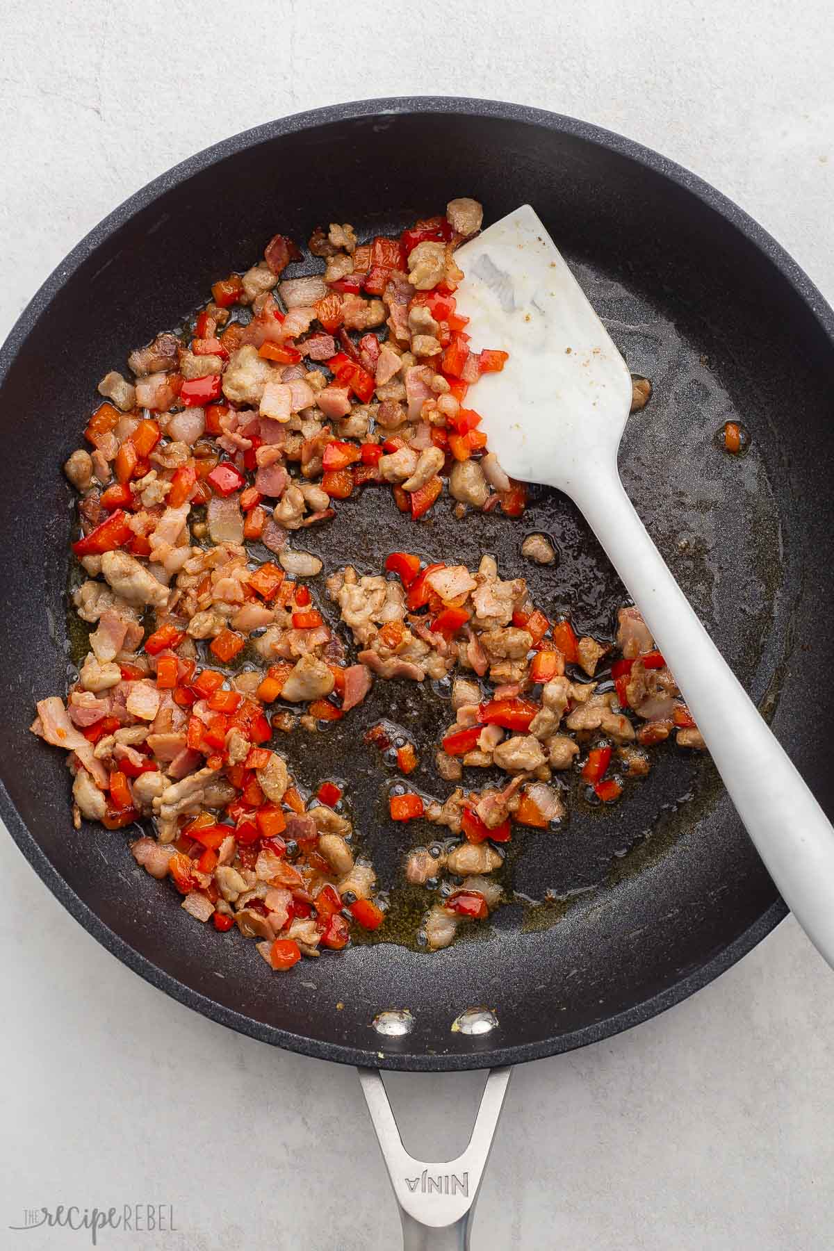 Top view of diced peppers and ground beef in a pan with a spatula. 
