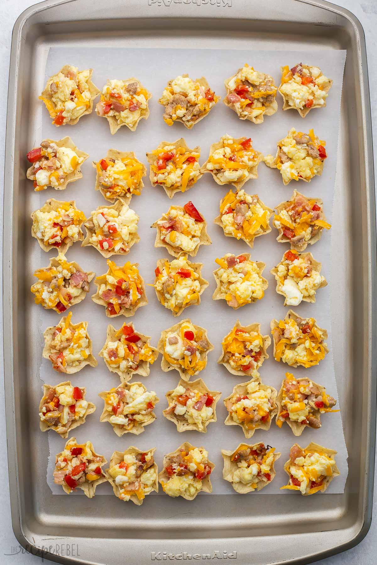 Top view of baking tray lined with parchment paper, filled with taco cups that have been filled with beef taco mixture and topped with cheese. 