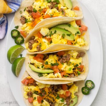 Top view of breakfast tacos on a white platter with jalapenos and limes.