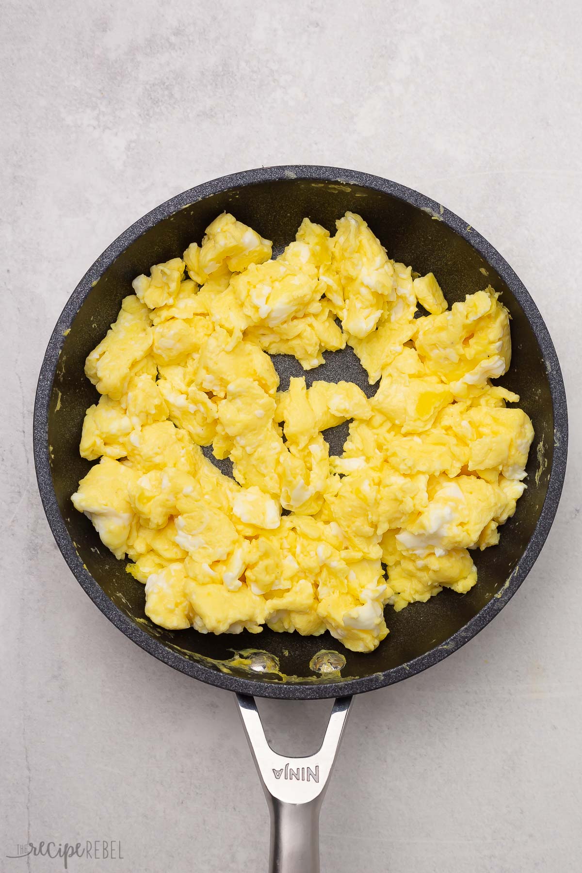 Top view of scrambled eggs in a black frying pan.