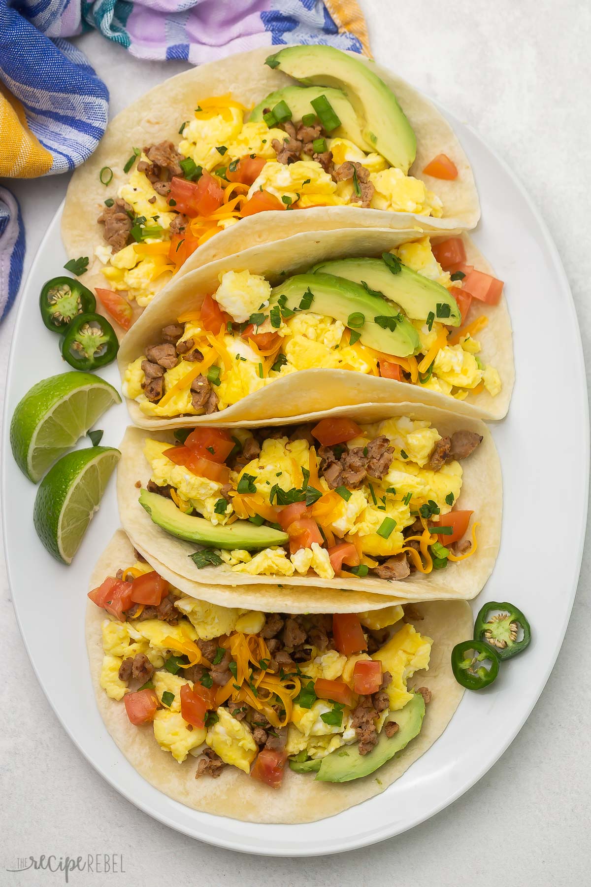 Top view of four breakfast tacos on a white platter with extra toppings placed beside.