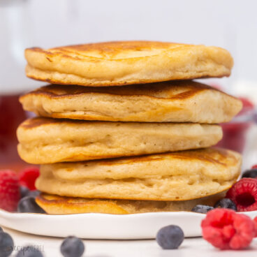 buttermilk pancakes stacked high on a white plate with berries around.